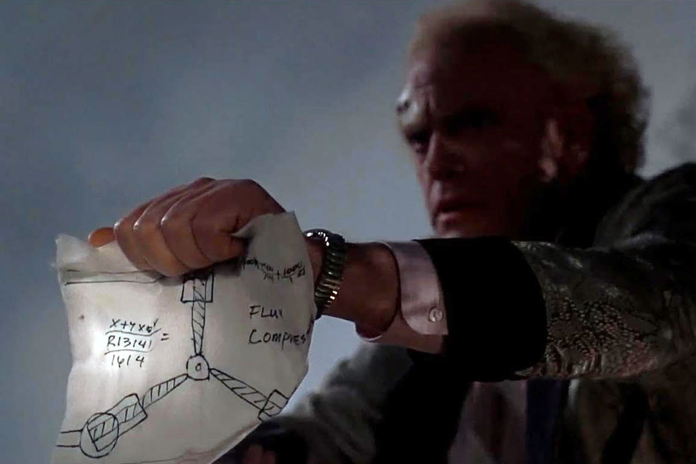 Christopher Lloyd als Dr. Emmett Brown mit einer Zeichnung des Flux-Kompensators